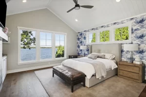 View of master bedroom area with vaulted ceilings finished in white shiplap, windows overlooking the lake and high windows above the bed to add additional light