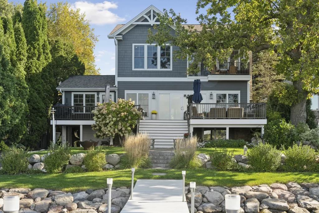 Photo of back of remodeled house with gray siding and white trim and a newly landscaped lawn with shrubs and a rock wall