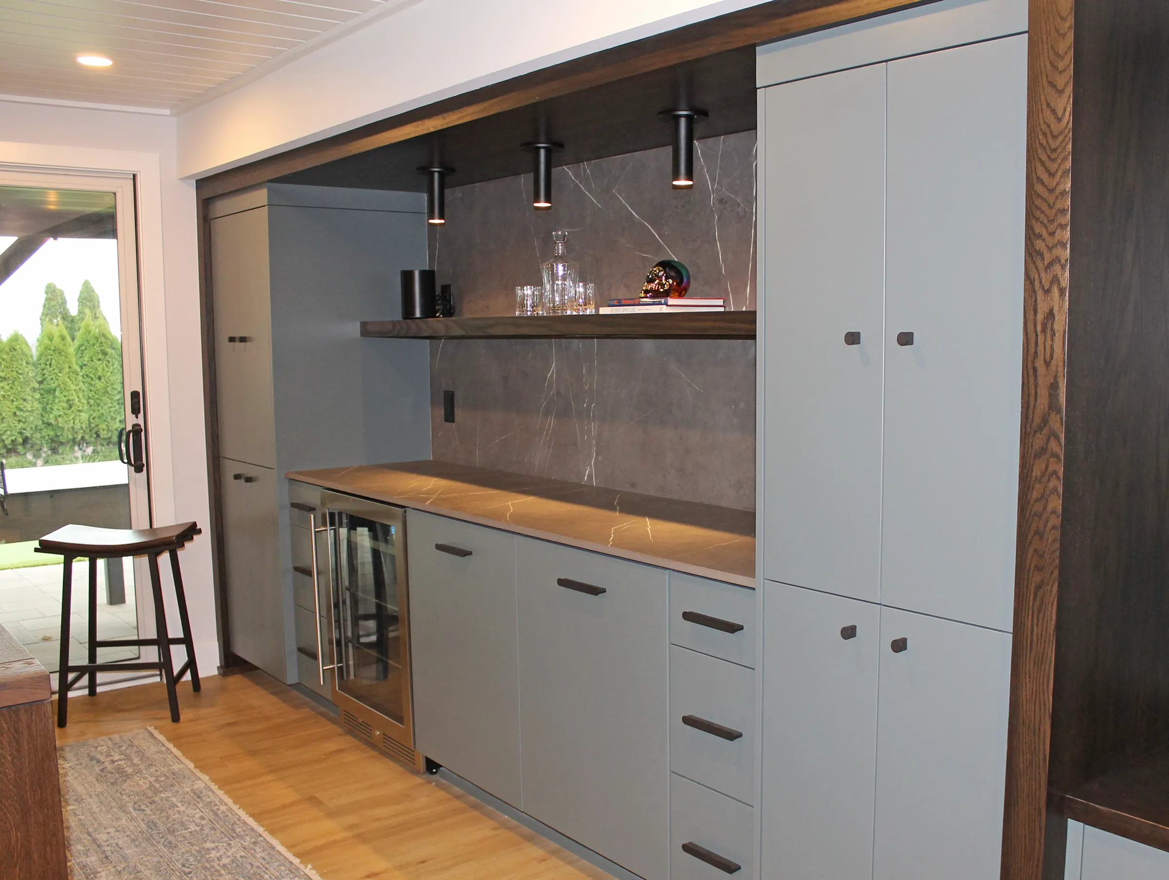 Built in bar in remodeled basement; gray with black hardware, built in lighting and wine refrigerator, granite backsplash and counter and wood shelf