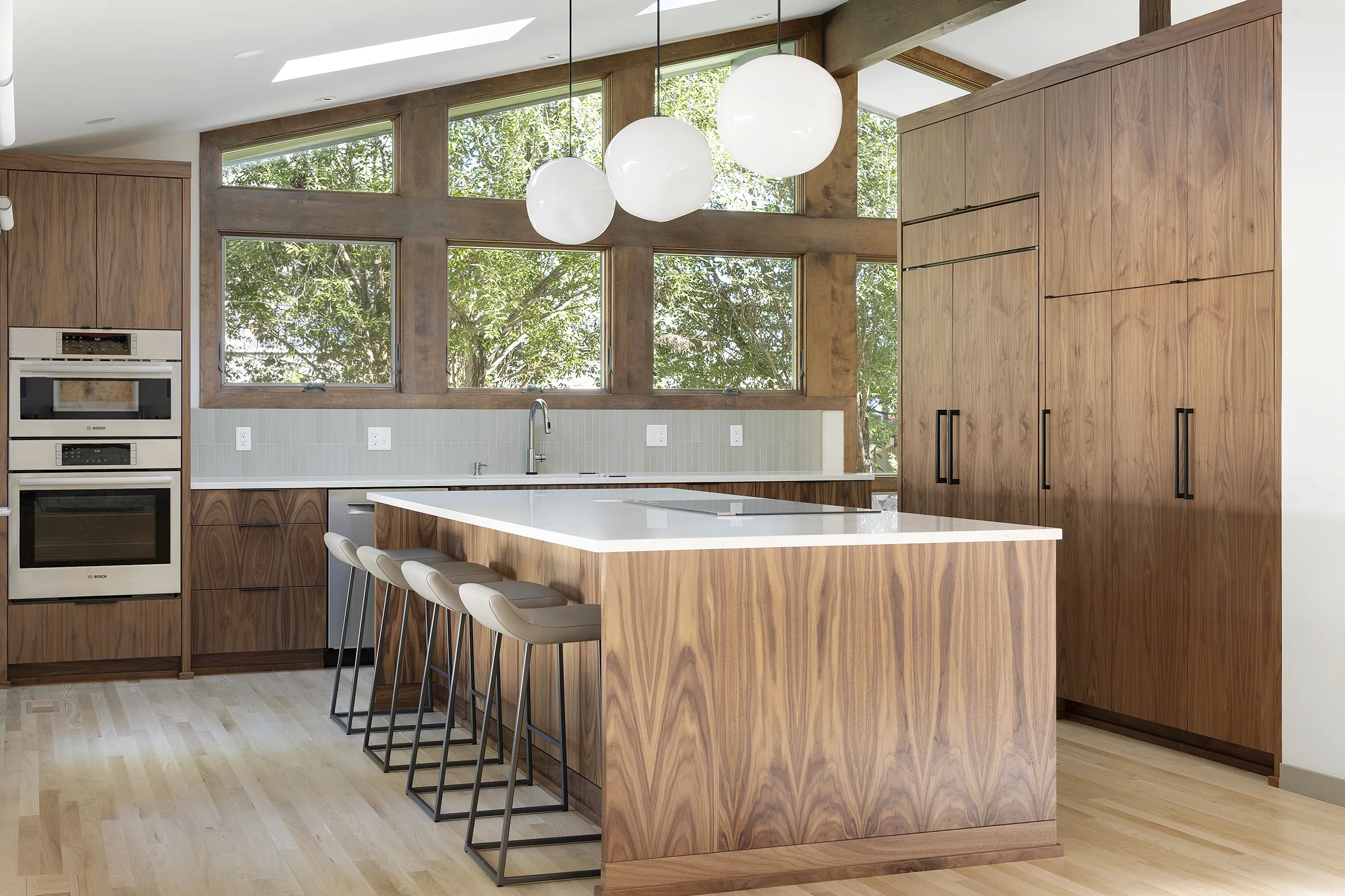 kitchen remodel with handmade globe lighting over large island; dark wood cabinets and window trim; light oak flooring throughout